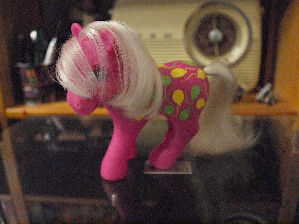 Pink Little Pony with side-swept blonde hair and green and yellow balloons on her hips