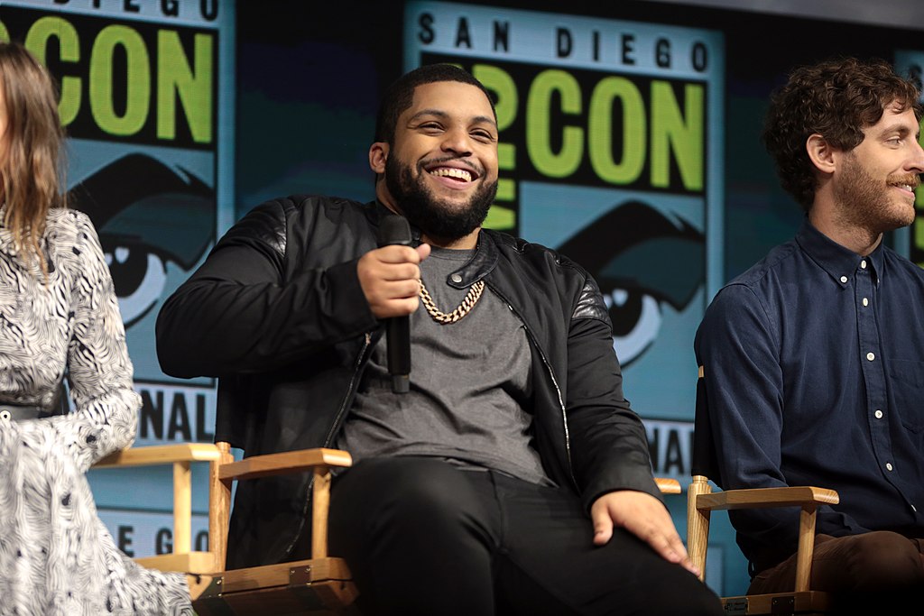 O'Shea Jackson assis entre deux personnes tout en tenant un micro sur. une main